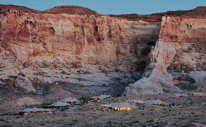 Amangiri's Camp Sarika nestled within rust-coloured canyon walls beside a flowing stream at dusk.