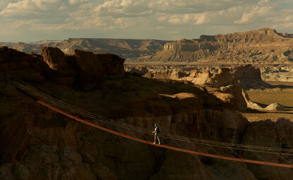 Climber traversing a via ferrata route across red rock formations at Amangiri.