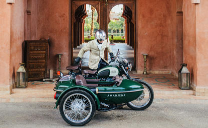 复古摩托车与边车停放在安缦珍纳度假村的赭红色建筑前。