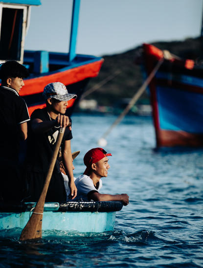 Child in shallow water beside traditional wooden fishing boats at Amanoi, Vietnam.