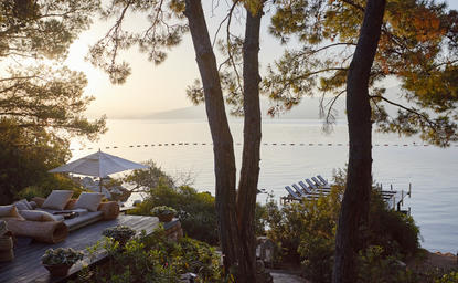 Bar area at Amanruya overlooking the Aegean Sea at dusk, framed by trees.