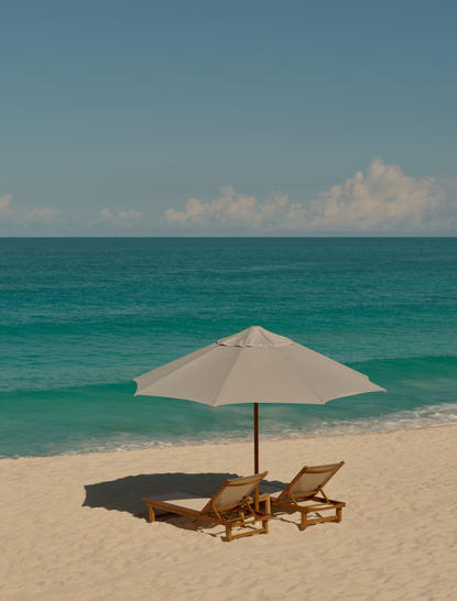 アマンヤラ リゾートのビーチで、白い傘の下に置かれた木製のサンラウンジャー