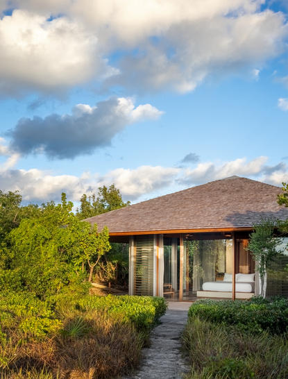 安缦涯澜度假村海湾馆外景，茅草屋顶建筑坐落于花园景观中。