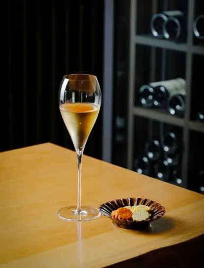 Glass of champagne beside a dark plate on a wooden table at Aman Kyoto.