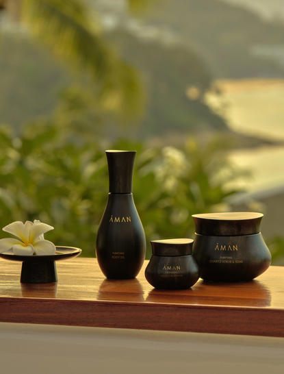 Spa essentials arranged on a wooden surface at Amanpuri resort, featuring dark ceramic vessels with water views beyond.