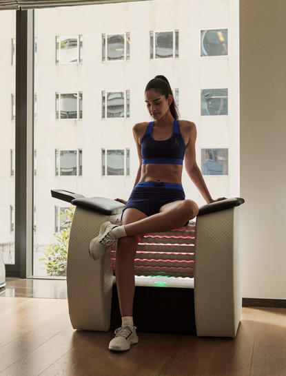 アマン ニューヨークのホテルロビーで、女性が木製のベンチに座っている。背後には白い壁に複数の窓枠が描かれている。