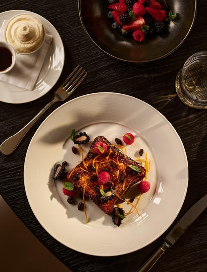 Breakfast plate at Aman New York featuring toast topped with tomatoes and berries, served with fresh fruit and coffee.
