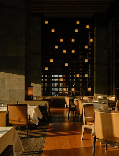 Salle à manger d'Aman Tokyo avec luminaires suspendus dorés et tables en bois.
