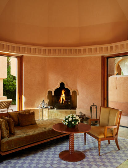 Fireplace in a curved pavilion at Amanjena, Morocco, with warm terracotta walls and mid-century furniture.