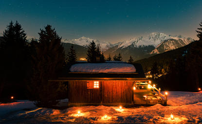 Aman Le Mélézin glows warmly at dusk, with snow-capped Alps rising beyond forested slopes.
