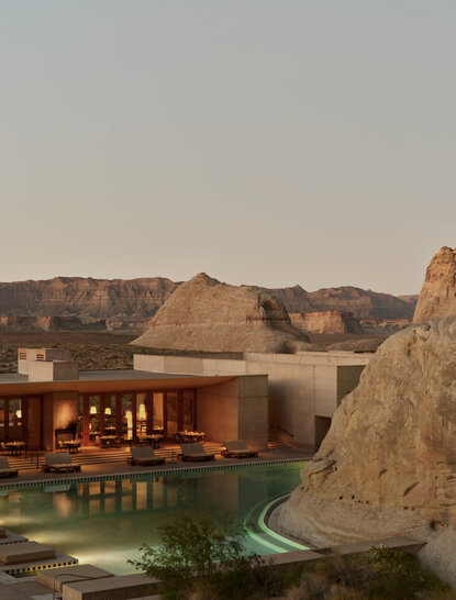 Amangiri resort exterior at dusk, with illuminated pavilions nestled against desert rock formations.