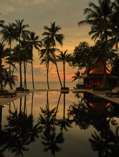 Piscina principale di Amanpuri al tramonto, con palme riflesse nell'acqua calma della resort in Tailandia.