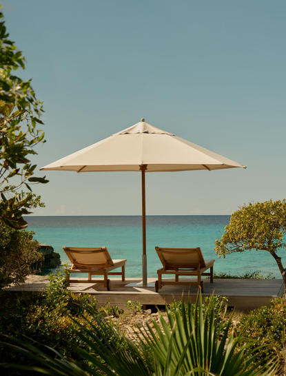 Sun loungers beneath a cream parasol overlooking turquoise waters at Amanyara, Turks and Caicos.