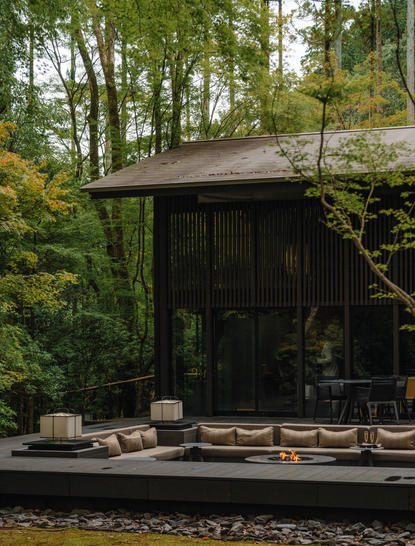 Aman Kyoto resort exterior with modern pavilion nestled amongst woodland trees and stone seating area.