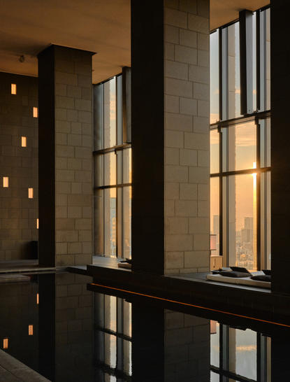 Spa wellness area at Aman Tokyo with tall windows overlooking the city, warm lighting and dark stone features.