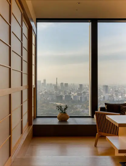 Deluxe room at Aman Tokyo with floor-to-ceiling window overlooking the city skyline, wooden panelling and minimalist décor.