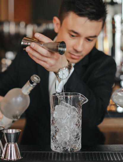 Bartender pouring a cocktail at Aman Venice's bar, concentrating on the drink preparation.