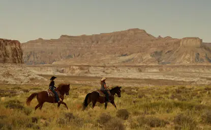 Two riders on horseback crossing the desert landscape at Amangiri, with rust-coloured mountains in the distance.
