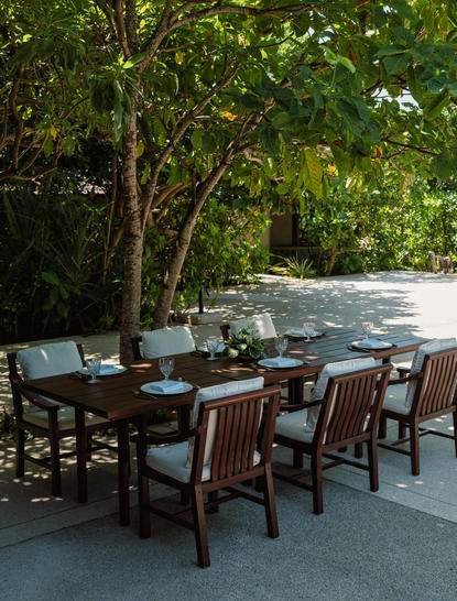 Outdoor dining area at Amanpulo resort with wooden table and chairs beneath tropical trees.