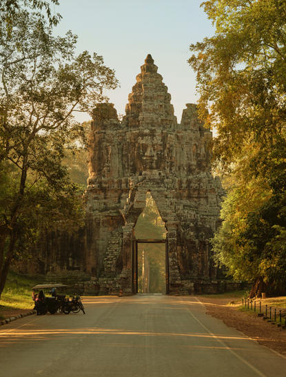 Remork parked at the entrance gate to Angkor temple, framed by ancient stone towers and tree-lined avenue at Amansara, Cambodia.
