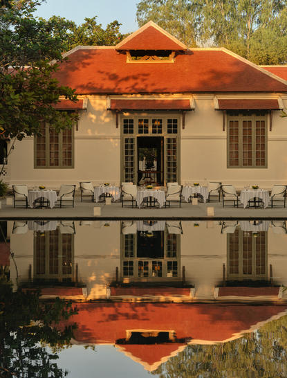 Amantaka's symmetrical colonial façade with terracotta roof reflected in still water below.