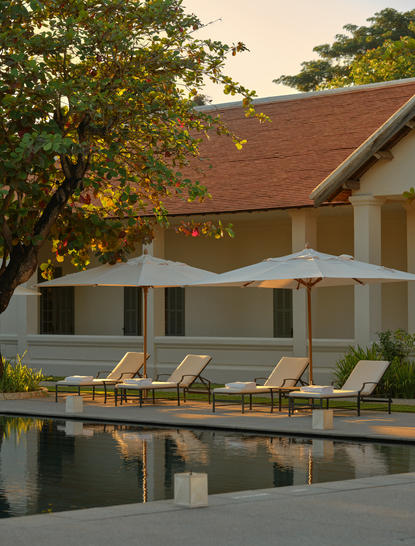 Amantaka's pool terrace at golden hour, with loungers reflected in still water and traditional architecture beyond.