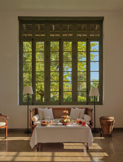 Afternoon tea service laid out on a table beneath tall windows at Amantaka, Laos, with library shelving visible above.