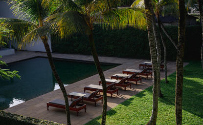 Wooden benches beside a plunge pool at Amangalla, surrounded by palm trees and manicured lawn.