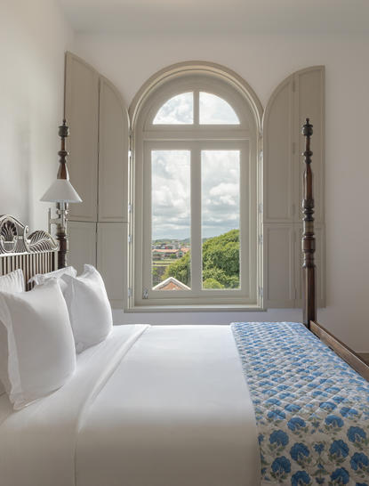 Principal bedroom at Amangalla with arched window overlooking Sri Lankan landscape.