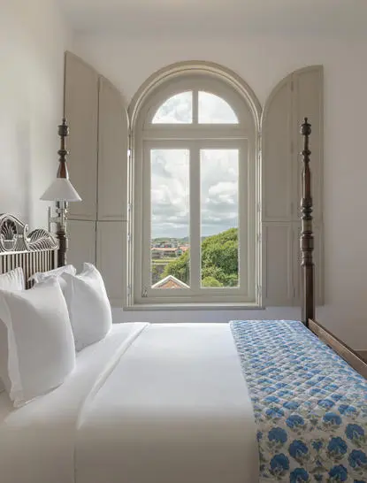 Principal bedroom at Amangalla with arched window overlooking Sri Lankan landscape.