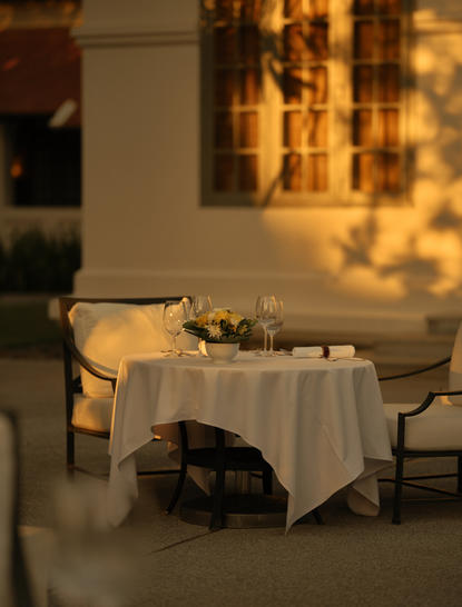 Candlelit poolside dining table at Amantaka, set for an intimate dinner beneath warm golden lights.