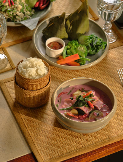 Amantaka dining: Lao set menu featuring curry and fresh herbs on woven table setting.