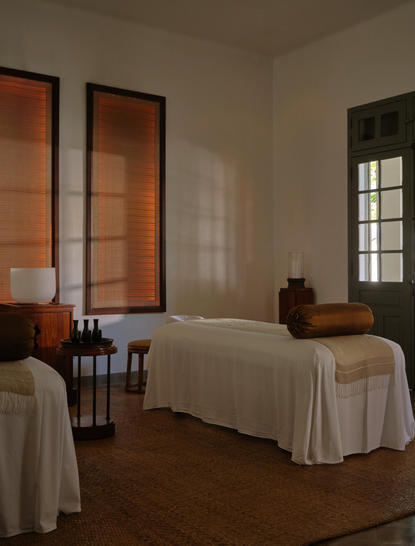 Double treatment room at Amantaka wellness spa, featuring two massage beds with cream linens and wooden partition screens.