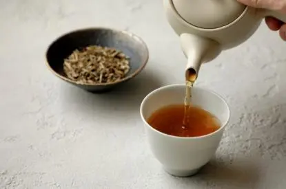Tea ceremony preparation at Aman Kyoto, with hot water being poured into a white cup beside a bowl of tea leaves.