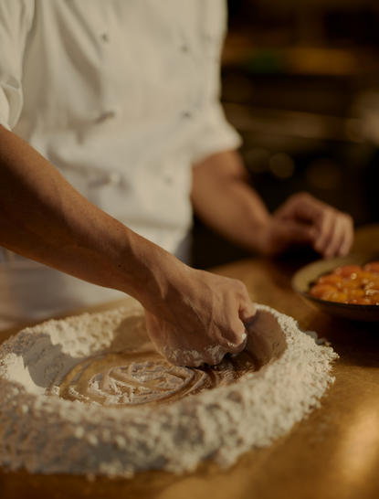 Hands kneading pasta dough during a cooking class at Aman New York hotel.