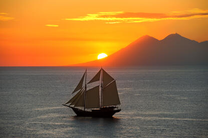Sailing vessel at sunset off the coast of Amandira, Indonesia, golden sky reflected on calm waters.