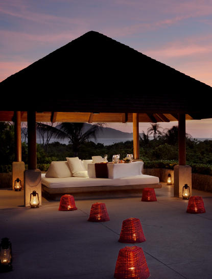 Salle à manger en plein air au coucher du soleil à Amanpulo, avec un pavillon éclairé et des lanternes rouges.