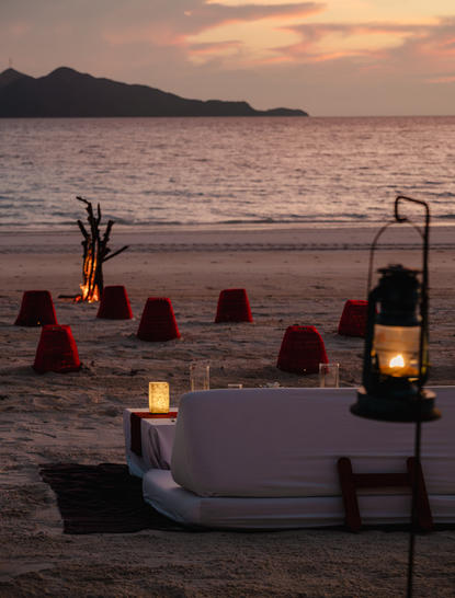 Candlelit private dining setup on the beach at sunset, Amanpulo resort.