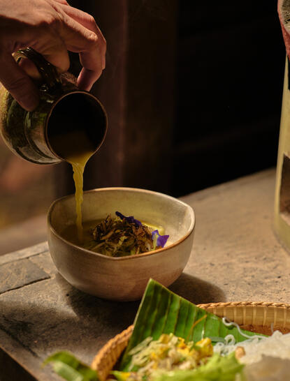 Green coconut curry being prepared at Amansara's Khmer dining venue, with broth poured over fresh rice noodles.