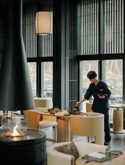Afternoon tea service at Aman Kyoto resort, with guest seated by floor-to-ceiling windows overlooking gardens.