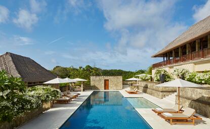 Rectangular swimming pool with loungers and umbrellas at Aman Villas at Nusa Dua, surrounded by manicured gardens and villa architecture.