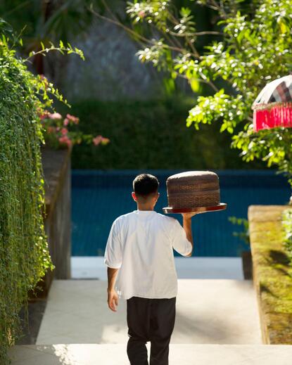 Butler carrying luggage through vine-covered pathway at Aman Villas at Nusa Dua.