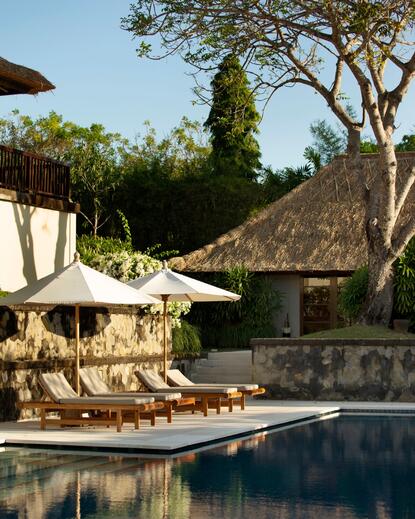 Private swimming pool at Aman Villas at Nusa Dua, with sun loungers and thatched structures.