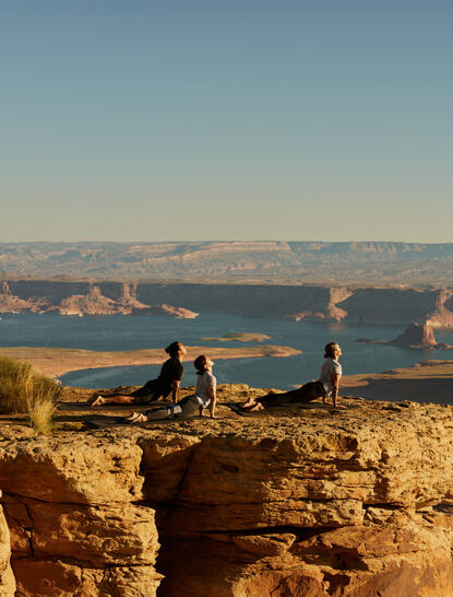 Deux personnes pratiquent le yoga sur une formation rocheuse dominant le lac Powell à Amangiri, resort du désert américain.