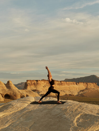 Yoga practitioner in warrior pose on rock formations at Amangiri, Utah, at sunset.