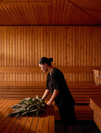 Wellness attendant arranging stones on wooden floor in forest banya at Amanoi resort.