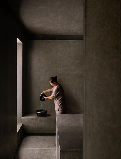 Amanoi-ის რეზორტში მცენარე ტიპის აბაზანაში ქალი რელაქსირებულია თოვლის აკვამარინის აუზის მახლობლად, რომელიც მოხვდება ღია საღამო სინათლეში.