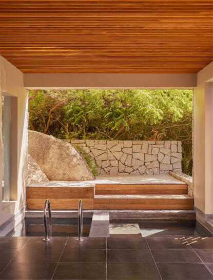 Amanoi resort에 위치한 호수 웰니스 풀 빌라의 외부 전망으로, 목재 천장 아래 돌담과 식생이 있는 휴식 공간을 보여줌.