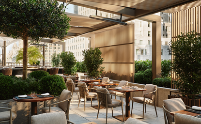 Garden terrace at Aman New York with dining tables, wooden chairs, and potted greenery under a modern canopy.