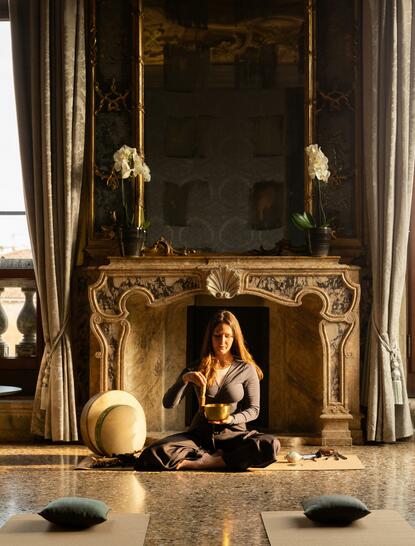 Sesión de curación sonora en la Sala Tiepolo del hotel Aman Venice, con chimenea dorada y velas encendidas.